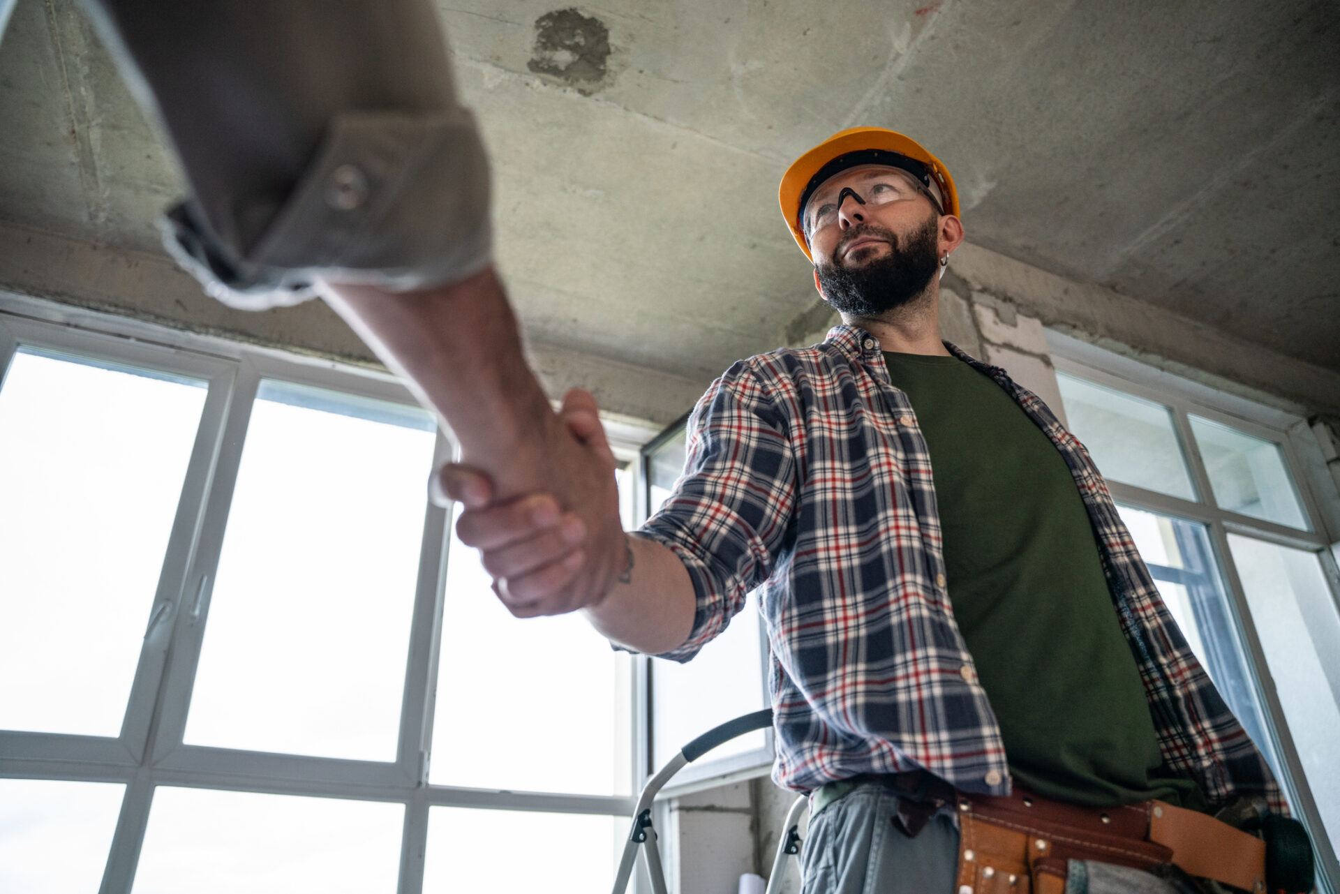 Handshake at construction site. Construction worker handshakes hands with a home owner Plumber in a hard hat and tool belt shaking hands with a homeowner inside a bright room under renovation, conveying professional plumbing service and a trusted local contractor relationship